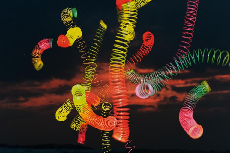 Neurologie: Colorful slinky springs are suspended in mid-air against a dark sunset background.