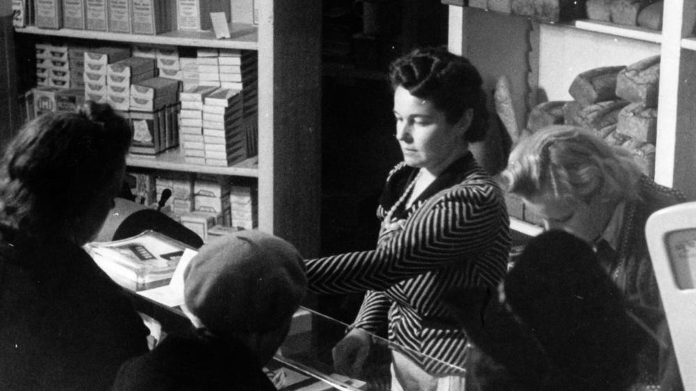 "Wie konnte das Geschehen?" von Götz Aly: Die Deutschen waren nicht kriegsbegeistert, sie profitierten jedoch vom Verbrechen: Ihre Versorgung verbesserte sich, weil man Millionen, allen voran sowjetische Soldaten, verhungern ließ, Millionen andere umbrachte. Das Motiv aus der nationalsozialistischen Propaganda zeigt einen Lebensmittelladen, um 1940.