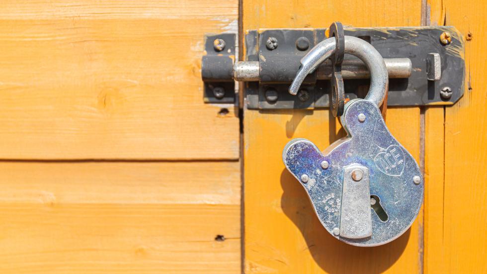 Ein offenes Vorhängeschloss hängt an einer gelben Holztür. 