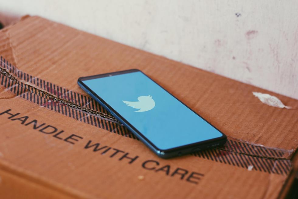 Smartphone mit Twitter-Logo liegt auf einem Karton mit der Aufschrift "Handle with care"