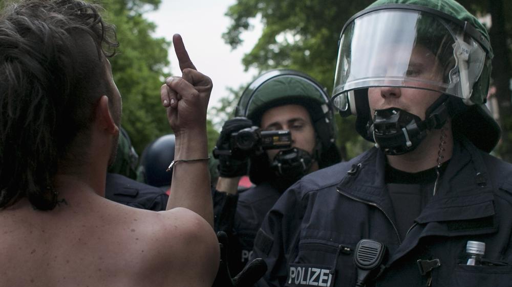 Polizeigewalt: 1. Mai in Berlin: Ein Demonstrant zeigt einem Polizisten den Mittelfinger.