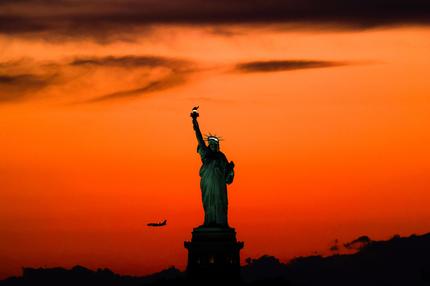 Sommerferien: The Statue of Liberty is seen at dusk while a passenger aircraft approaches Newark airport in New York on August 11, 2024. (Photo by CHARLY TRIBALLEAU / AFP) (Photo by CHARLY TRIBALLEAU/AFP via Getty Images)