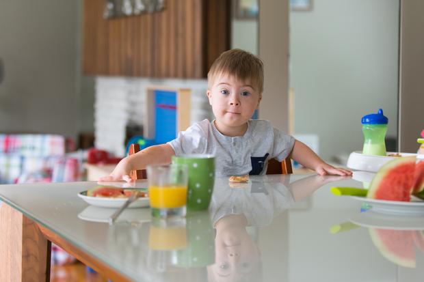 Ein Zweijähriger mit Down-Syndrom an einem Esstisch. Er lebt in Kanada