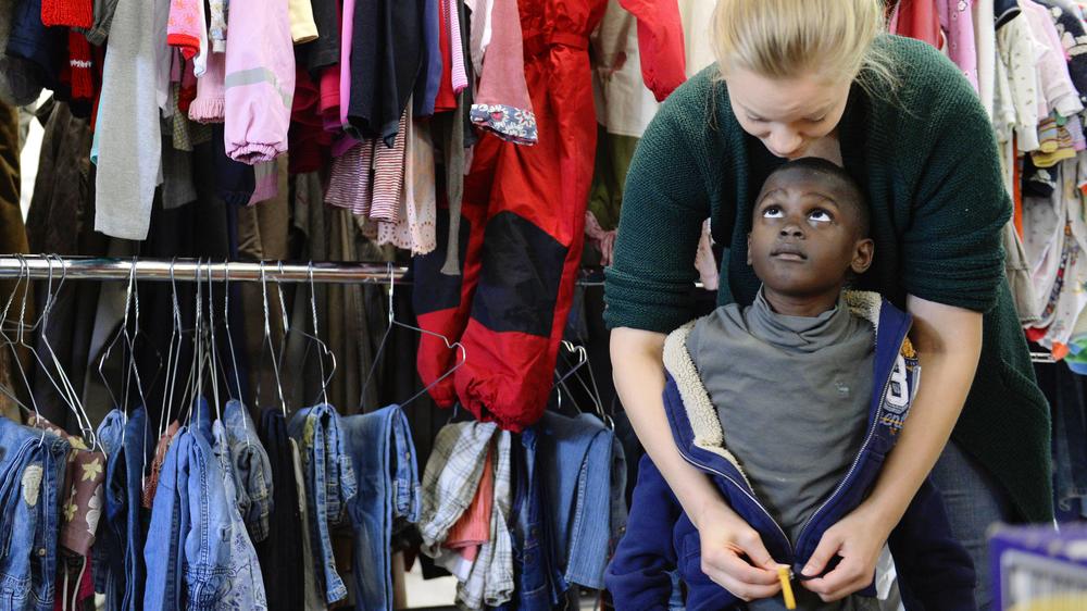 Wie Sie Flüchtlingen helfen können: Helferin und Flüchtlingskind in der Kleiderkammer der "Bayernkaserne"