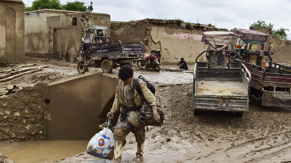 Unwetter: Ein afghanischer Mann trägt seine Habseligkeiten durch eine schlammbedeckte Straße, die nach einer Sturzflut im Dorf Laqiha in der afghanischen Provinz Baghlan überschwemmt wurde. 