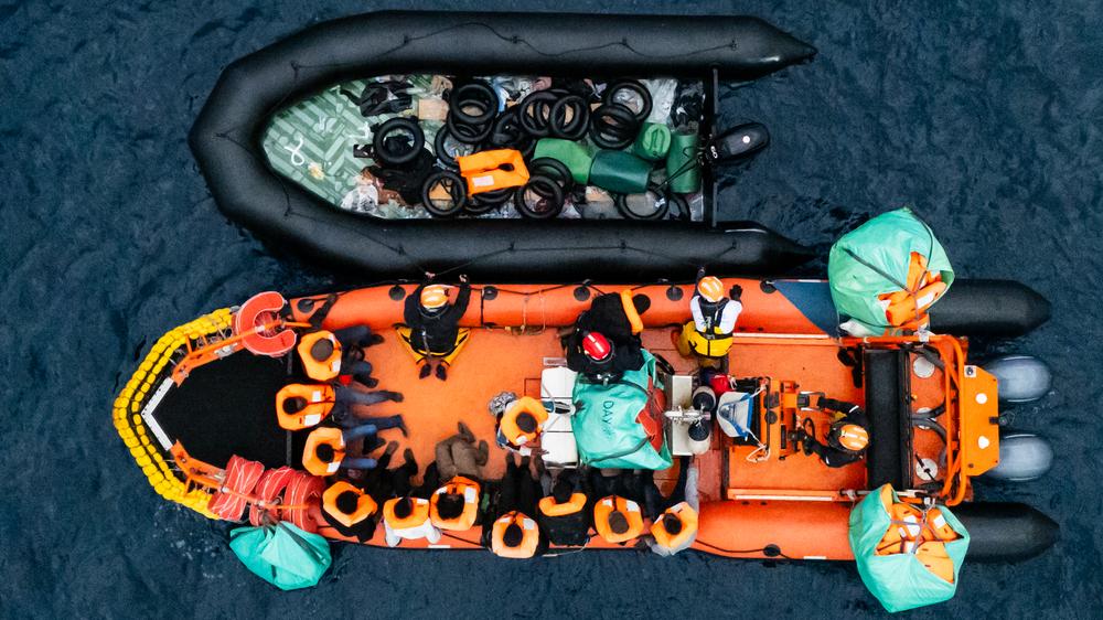 Migration: Ein Rettungsboot sichert ein Boot mit Geflüchteten, die das Mittelmeer überqueren wollten.