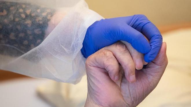 Gesundheit: Eine Altenpflegerin in Schutzkleidung hält die Hand eines Bewohners.