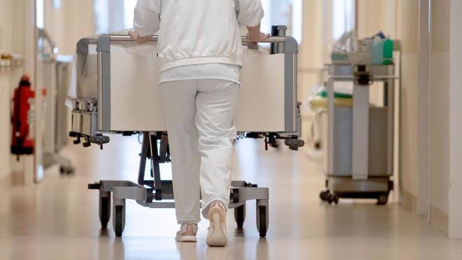 Krankenhäuser: Eine Krankenpflegerin schiebt ein Krankenbett durch einen Flur.