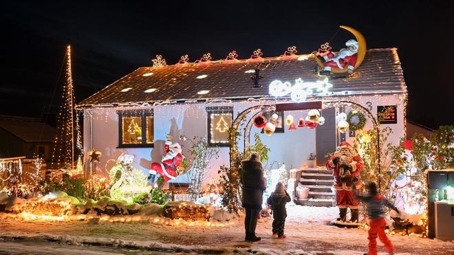 Brauchtum: Eine Frau steht mit zwei Kindern vor einem beleuchteten Weihnachtshaus.