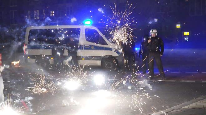 Bevölkerung: Polizeibeamte stehen am Silvesterabend hinter explodierendem Feuerwerk.