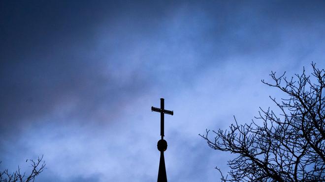 Brauchtum: Dunkle Wolken ziehen über das Kreuz auf einer Kirche hinweg.
