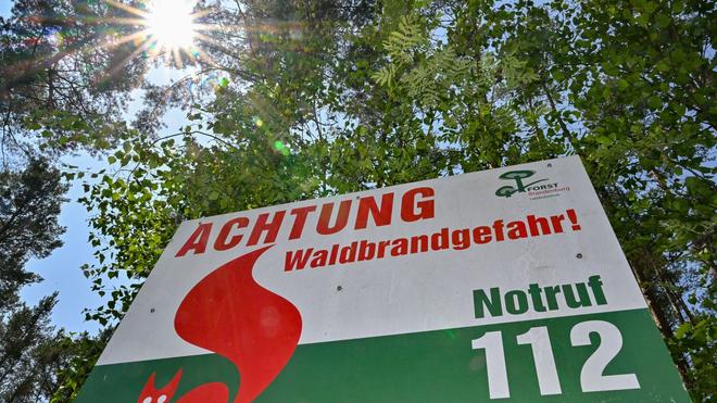 Natur: Ein Schild vom Landesbetrieb Forst Brandenburg met het Aufschrift «Achtung Waldbrandgefahr!  Notruf 112» steht voor Bäumen.