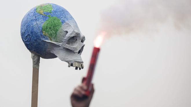 Demonstrationen: Ein Rauchfackel wird vor einer Weltkugel mit Knochengesicht gezündet.