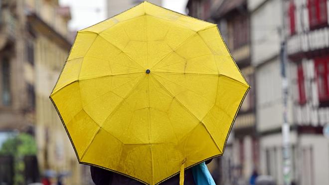 Wettervorhersage: Ein Passant mit gelbem Regenschirm.