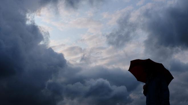 Wetter: Ein Mann geht mit einem Regenschirm vor aufziehenden dunklen Wolken spazieren.