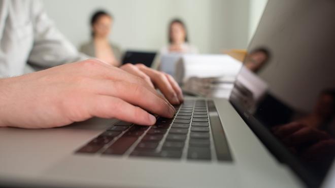 Quartalszahlen: Ein Mann tippt einem Büro auf einer Tastatur eines Laptops.