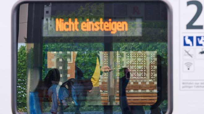 Bahn: Ein Bahnreisender schaut am Hauptbahnhof auf sein Smartphone, während in der Anzeige im Fenster eines Zuges „Nicht einsteigen“ zu lesen ist.