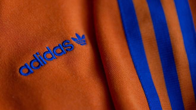 Sportartikel: Das Logo des Sportartikelherstellers adidas in blau auf einer orangen Jacke.