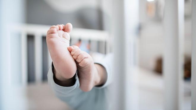 Sprachforschung: Die Füße eines Babys sind in einem Kinderbett zu sehen.