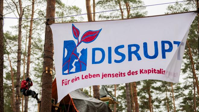 Grünheide: Ein Banner mit der Aufschrift  «Disrupt - für ein Leben jenseits des Kapitalismus» hängt im Camp der Initiative «Tesla stoppen» in einem Kiefernwald nahe der Tesla-Gigafactory Berlin-Brandenburg zwischen Bäumen.
