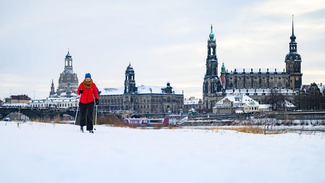 Fotografie: Eine Frau läuft am verschneiten Elbufer vor der historischen Altstadtkulisse in Dresden Ski