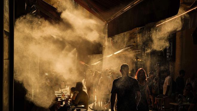 Fotografie: Menschen laufen unter Sprinklern eine Straße in Nizza entlang während einer Hitzewelle an der französischen Riviera.