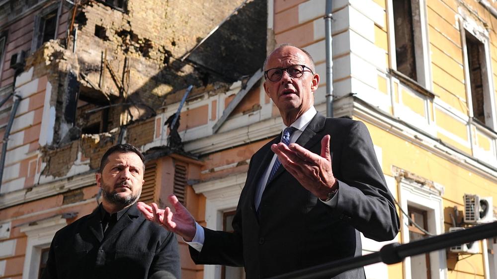 Krieg in der Ukraine: Bundeskanzler Friedrich Merz (rechts, CDU) und Wolodymyr Selenskyj (links), Präsident der Ukraine, stehen vor dem zerstörten Gebäude der Nationalen Akademie der Wissenschaften.