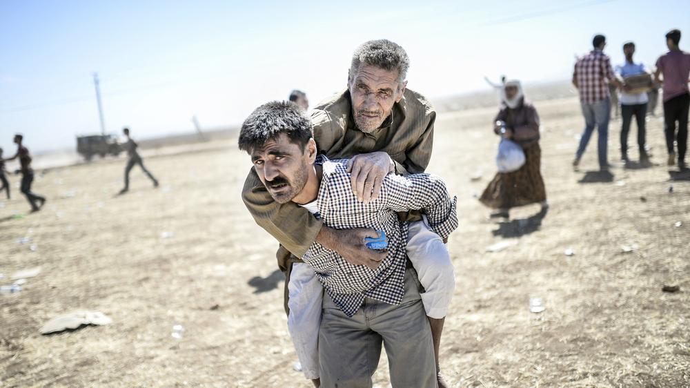 Ein Mann trägt einen älteren syrischen Kurden in der Nähe der türkisch-syrischen Grenze