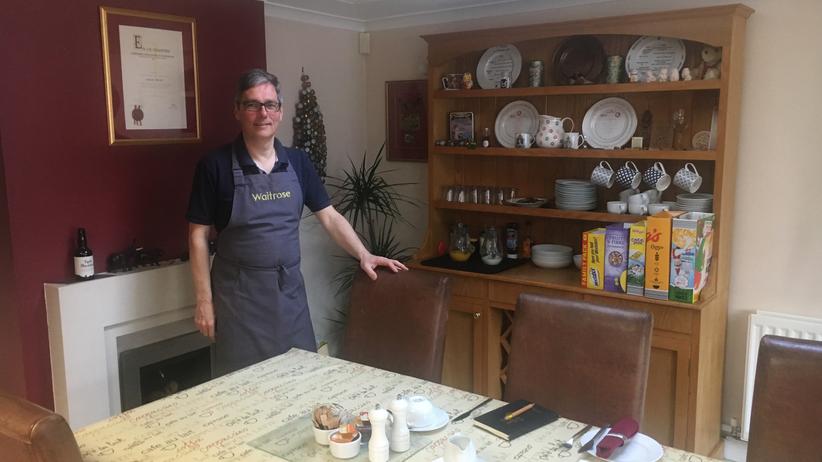 Laurent steht vor dem Esstisch, an dem sich Jane, Richard und Michael für das Brexit-Dinner zur Debatte getroffen haben.