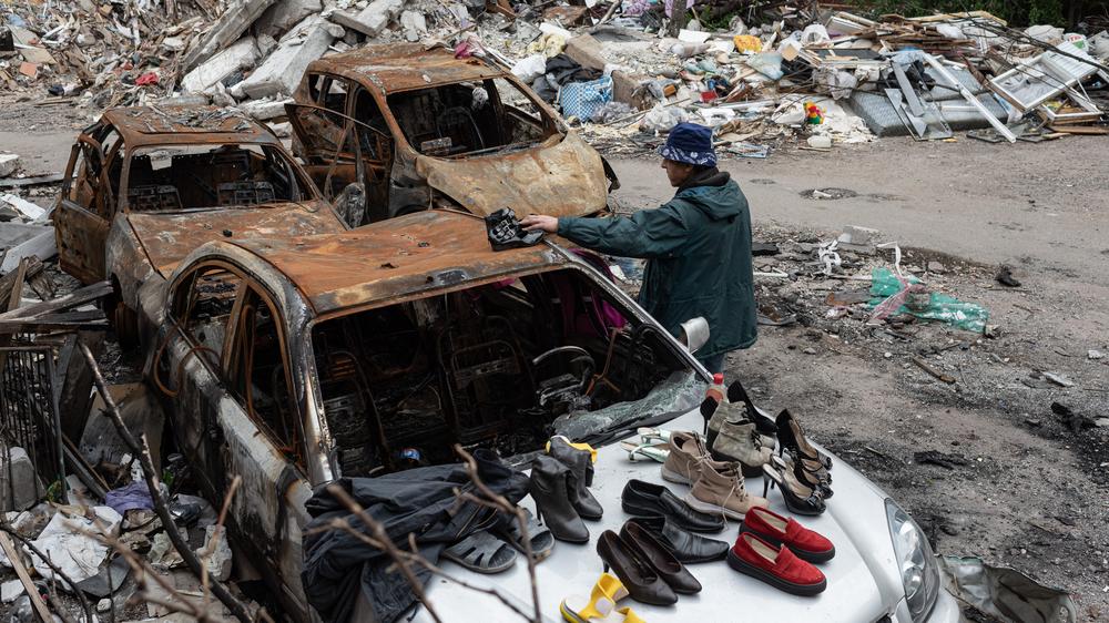 Ukraine-Überblick: Ein Mann in der kriegszerstörten nordostukrainischen Stadt Tschernihiw begutachtet Schuhe, die jemand auf einem ausgebrannten Auto für Passanten zum Mitnehmen aufgereiht hat.
