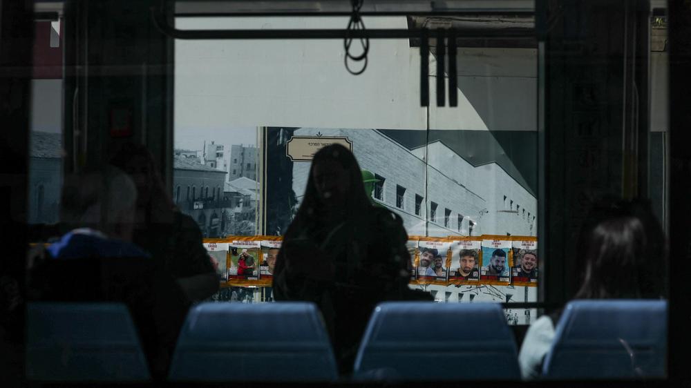 Gazastreifen: Menschen fahren am 3. Mai 2024 mit einer Stadtbahn durch Jerusalem, während durch ein Fenster Plakate der Geiseln zu sehen sind.