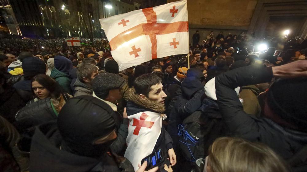  Demonstranten mit der georgischen Nationalflagge ziehen vor das Parlamentsgebäude in Tbilissi