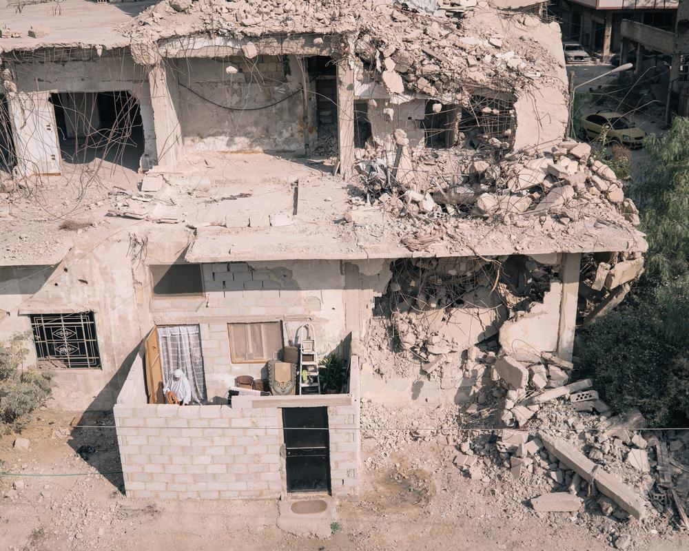 Syrien: A woman is seen in the frontyard of an apartment in a heavily damaged building.