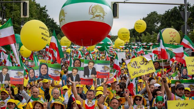 Demonstrantinnen und Demonstranten halten Schilder hoch, auf denen die Anführer der Volksmudschahedin abgebildet sind