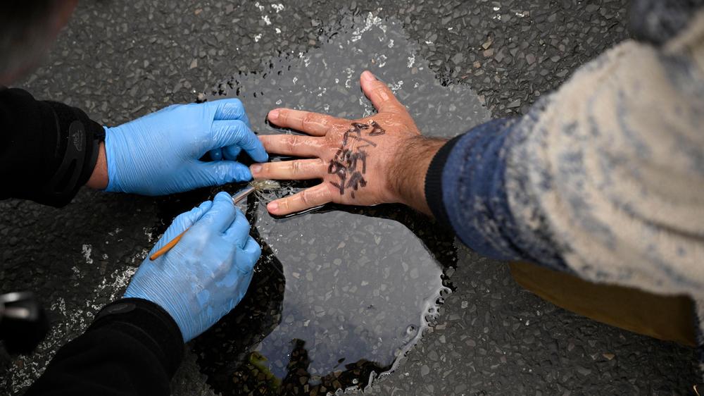 Klimaaktivisten: Ein Polizist löst die Hand eines Mannes, der sich an der Straße festgeklebt hat, vom Asphalt ab.