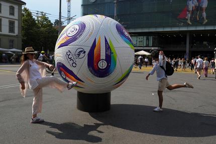 Spielplan der Fußball-EM: Menschen posieren für ein Foto vor einem riesigen Fußball, der vor dem Bahnhof Bern anlässlich der Frauenfußball-Europameisterschaft 2025 ausgestellt ist.