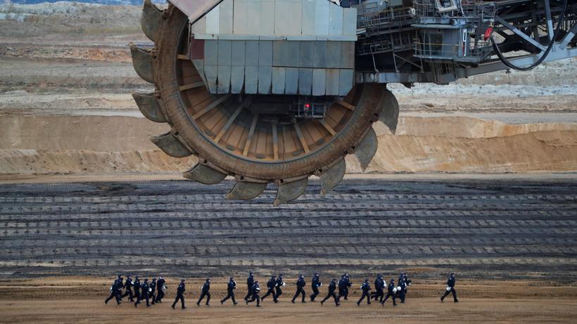 Klimapolitik: Polizisten rennen im Tagebau von Garzweiler, Nordrhein-Westfalen, an einem Braunkohlebagger vorbei. Das Bild entstand im November 2017, als Aktivistinnen und Aktivisten in die Kohlegrube eindrangen. 