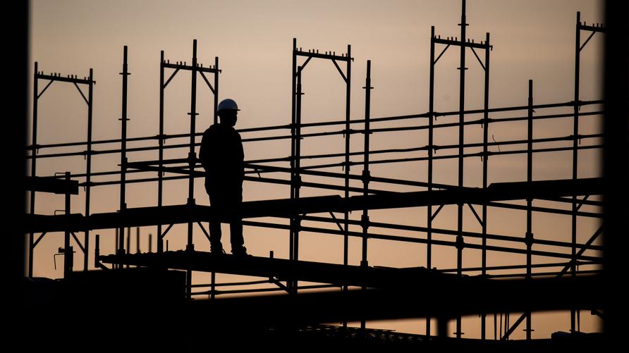 Konjunktur: Die Silhouette eines Bauarbeiters zeichnet sich auf einer Baustelle vor dem verfärbten Morgenhimmel ab. (zu dpa: «Mehr Erwerbstätige in Hessen 2023 als bislang angenommen») +++ dpa-Bildfunk +++