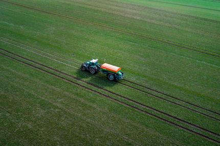Beschluss der Mindestlohnkommission: Mit einem Traktor zieht ein Landwirt einen Düngerstreuer zum Beginn der Agrarsaison über einen Acker. (Luftaufnahme mit einer Drohne) Bauern, Wissenschaftler und Politiker treffen sich am 26.02.2026 in Linstow zum Landwirtschaftstag der Volksbanken Raiffeisenbanken.