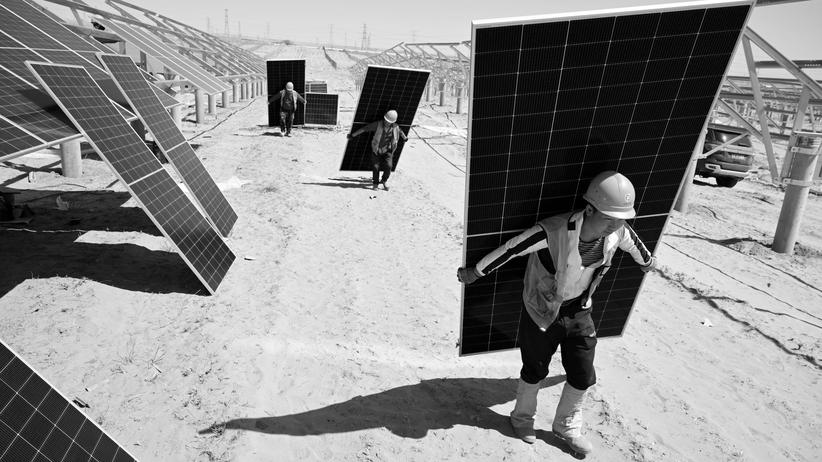 Krisenpodcast "Auch das noch": In der Wüste in Lingwu tragen Arbeiter die Paneele für eine der vielen neuen chinesischen Solarfarmen.