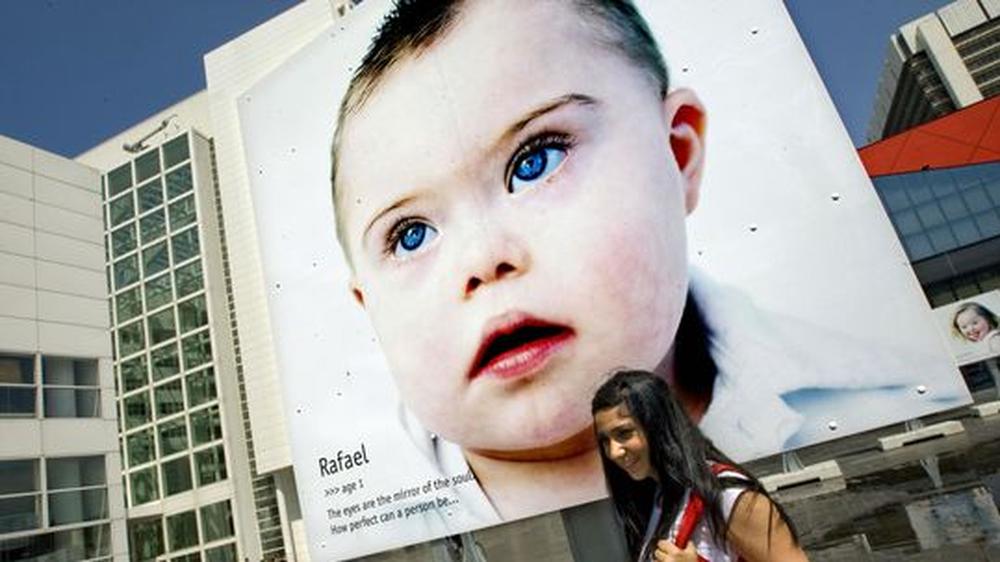 Von einem Plakat in Den Haag schaut ein Kind mit Trisomie 21 hinunter. Die Fotografin Eva Snoijink stellte 2009 Portraits von Kindern mit dem Down-Syndrom aus, um zu zeigen, dass sie ihr Leben genießen.