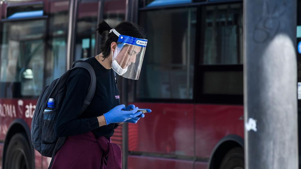 Atemschutzmasken: Eine Reisende mit einem Visier – vor einer Infektion mit dem Coronavirus schützt sie sich selbst und vor allem ihre Umwelt damit aber nicht.