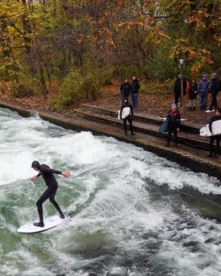 Eisbachwelle: Surfers gather to ride the famous Eisbach wave in the English Garden in Munich, Germany, on November 15, 2024. Dressed in wetsuits to ward off the cold, they showcase their skills on this artificial wave, a popular spot for urban surfing year-round. Autumn leaves add a vibrant backdrop, and a small crowd of spectators watches the surfers' daring maneuvers. (Photo by Michael Nguyen/NurPhoto via Getty Images)