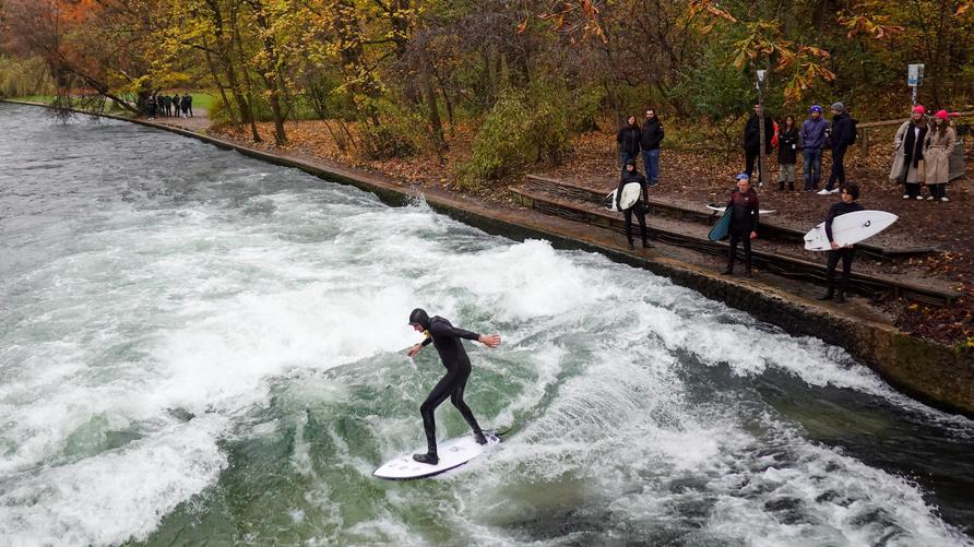 Eisbachwelle: Surfers gather to ride the famous Eisbach wave in the English Garden in Munich, , on November 15, 2024. Dressed in wetsuits to ward off the cold, they showcase their skills on this artificial wave, a popular spot for urban surfing year-round. Autumn leaves add a vibrant backdrop, and a small crowd of spectators watches the surfers' daring maneuvers. (Photo by Michael Nguyen/NurPhoto via Getty Images)